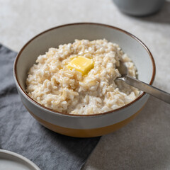 Unusual healthy delicious rice pudding made from brown rice and plant based milk served with butter and honey in grey bowl