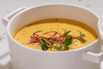 Pumpkin cream soup served with herbs in ceramic pot with lid