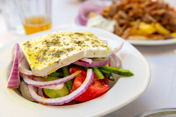 Traditional Greek Salad served in tavern, traditional greece food with Aegean sea as background. Tomatoes, cucumber, onions, olives, peppers, cappers and olive oil