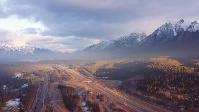 Canmore Alberta mountain range Canadian rockies surrounding highway and overpass aerial sunrise drone shot pan away.