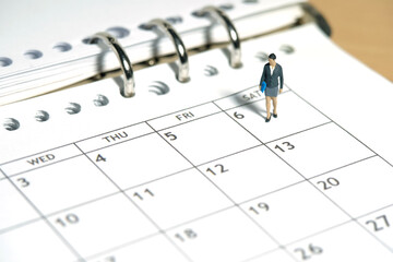 Miniature people toy figure photography. Work schedule concept. A businesswoman standing walking above calendar monthly planer. Isolated on white background.