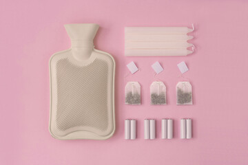 Hot water heating pad, tea bags, candles and batteries are winter essentials on pink background....