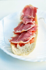 Breakfast toast of cured ham with the bread served on a white plate on a white table. Close-up