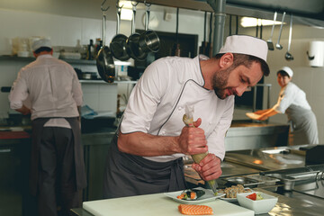 Professional Male Chef in uniforms preparing sushi in a kitchen of asian restaurant