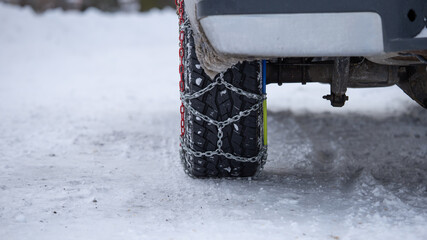 Car wheel with traction chains on a snowy road. SUV with tyre anti-skid snow chains.