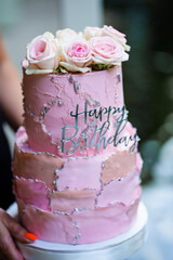 Beautiful two-tier pink cake with rosebuds and the inscription happy birthday. 