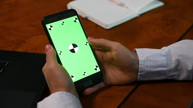 Close-up hands hold smartphone. Green chroma key. Copy ad space. Video for insert promotional clip or movie. Mock-up screen. Swiping Scrolling Internet Social Networks Browsing News Financial Reports
