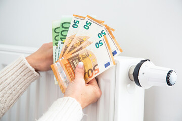 Radiator with thermostat and euro money banknotes in woman hands. Expensive gas heating costs concept. High home heating bills in Europe.