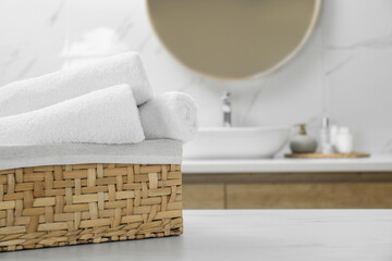 Fototapeta na wymiar Wicker basket with rolled bath towels on white table in bathroom, space for text