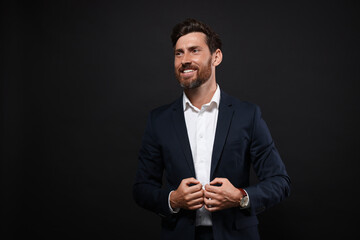 Portrait of smiling bearded man in suit on black background. Space for text