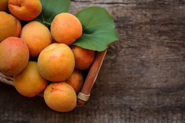 Basket with delicious ripe apricots on wooden table, top view. Space for text