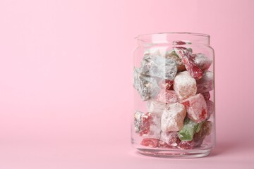 Delicious candies in glass jar on pink background. Space for text