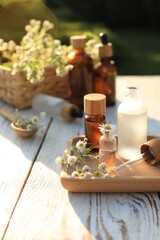 Fototapeta na wymiar Chamomile essential oil, pipette and flowers on white wooden table outdoors