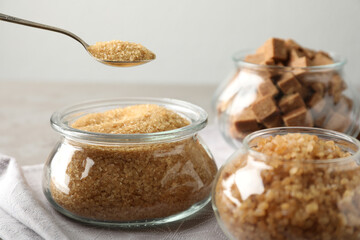 Taking spoon of brown sugar from glass bowl on table