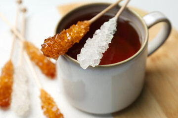 Sticks with sugar crystals and cup of tea on table, closeup