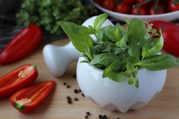 Mortar with different fresh herbs and pepper on wooden table, closeup