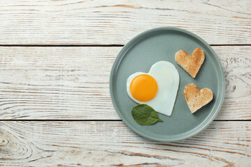 Romantic breakfast with heart shaped fried egg and toasts on white wooden table, top view. Space for text