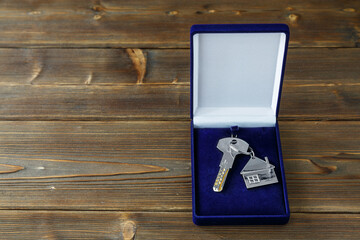 A key with a keychain in a gift box on a wooden table. Space for text. The concept of buying a house, apartment, housewarming.