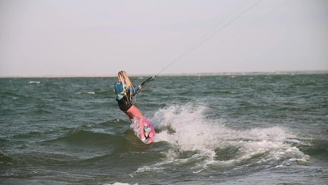 Slow motion on a telephoto lens. Young female athlete rides on a kiteboard in windy weather on big waves