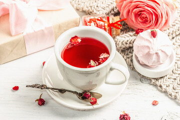 The concept of romantic tea. Wrapped gift, hibiscus tea, a bouquet of delicate roses, sweets