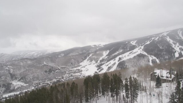 Aerial revealing over pine trees to Beaver Creek Ski Village, Colorado in winter viewing ski runs
