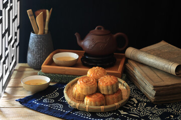 Homemade moon cakes on table and tea pot and cup set at the dark background with light shed from side window - dark and moody photography
