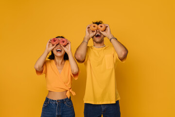 Young happy woman and enthusiastic man holding donuts on eyes