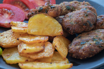Cyprus meatballs, tomatoes, french fries, peppers. Beautiful presentation on a black plate.