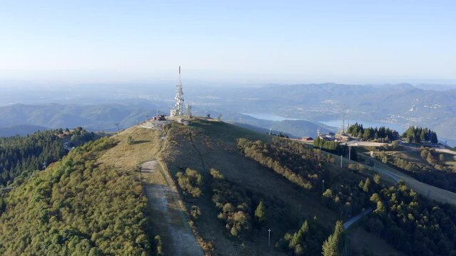 Telecommunications antenna complex on top of Mottarone mountain with lake in background, Stresa in Piedmont. Italy. Aerial descending. Sky for copy space