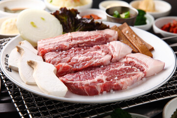 Korean table setting with grilled pork golden brown on the grill and side dishes set 그릴 위 노릇노릇하게 돼지고기를 굽고 있고 반찬이 세팅되어 있는 한상차림