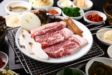 Korean table setting with grilled pork golden brown on the grill and side dishes set 그릴 위 노릇노릇하게 돼지고기를 굽고 있고 반찬이 세팅되어 있는 한상차림
