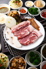 Korean table setting with grilled pork golden brown on the grill and side dishes set 그릴 위 노릇노릇하게 돼지고기를 굽고 있고 반찬이 세팅되어 있는 한상차림