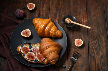 Croissants with cream cheese, figs, blueberries and honey on a black plate. Breakfast concept, top view.