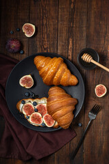 Croissants with cream cheese, figs, blueberries and honey on a black plate. Breakfast concept, top view.