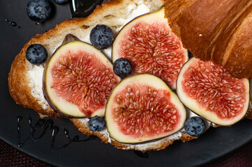 Croissants with cream cheese, figs, blueberries and honey on a black plate. Breakfast concept, top view.