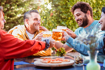 Group of friends toasting beer glasses and having fun outdoors - People having lunch in the garden...