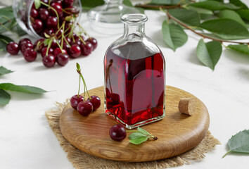 Glass bottle of homemade cherry brandy liqueur or wine with bunch of ripe berries on a light...