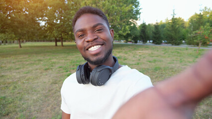 African American man records video smiling and standing in green park. Black guy with modern...