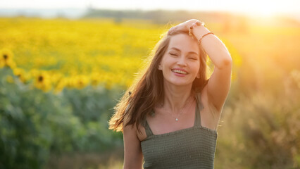 Woman wearing green dress runs past blooming sunflower field. Brown-haired lady enjoys life looking with smiling expression against blurry countryside