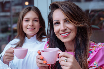 Happy smiling ladies sitting together outdoors in cafe and enjoying drinking tea from pink cups...
