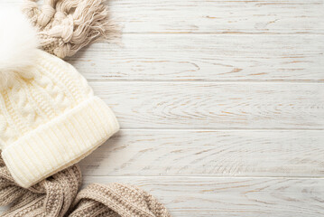 Winter concept. Top view photo of white bobble hat and knitted scarf on white wooden table...