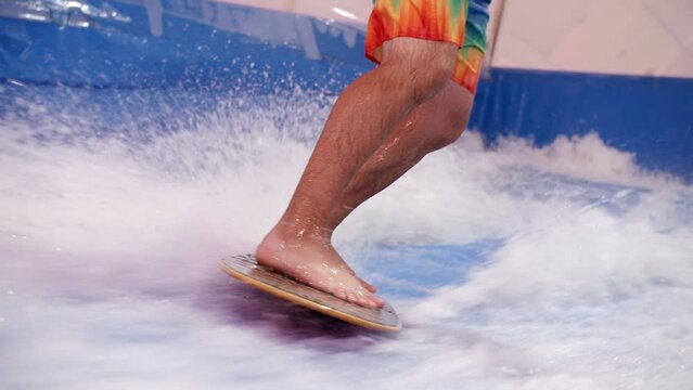 Attractive Man riding surf board on wave simulator indoors. Young surfer during training on generated waves. Water sport activity. Surfer guy enjoy surfing on indoor surf imitator.Close-up