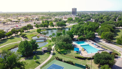 Tennis court and swimming pool sport complex in recreation park with small pond and downtown...