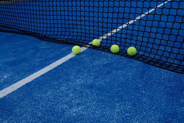 various balls by the net on a blue paddle tennis court
