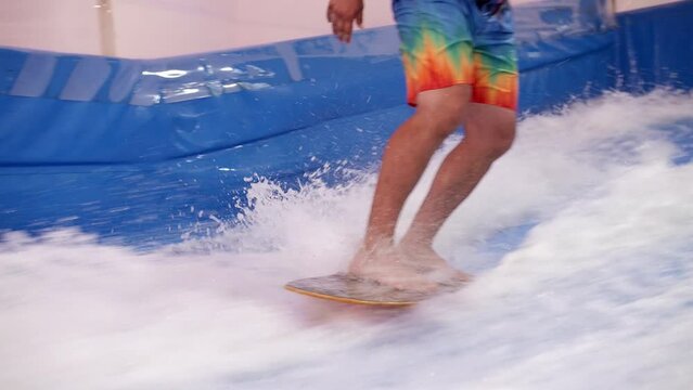 Attractive Man riding surf board on wave simulator indoors. Young surfer during training on generated waves. Water sport activity. Surfer guy enjoy surfing on indoor surf imitator.Close-up