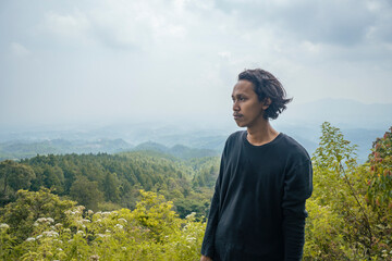 The young man smiling then stand and look on the peak of mountain. The photo is perfect for nature background, holiday poster and advertising.