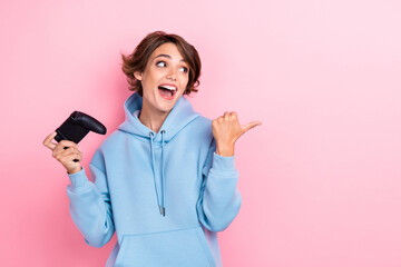 Fototapeta premium Photo of young adorable gorgeous cute woman wear blue hoodie hold joystick player online console finger pointing look empty space crazy isolated on pink color background