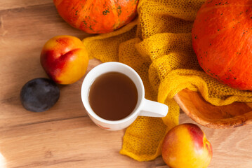 cup of tea with an autumn decor of pumpkins, plums, textiles and peaches on a wooden background