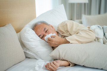 Senior man sneezing due to discomfort while lying in bed at home,Healthcare,Flu,Hygiene and people concept.