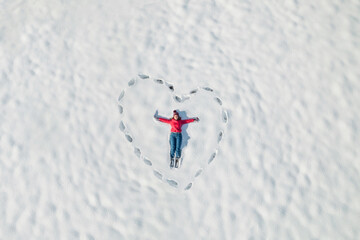 Woman lying on the snow in a heart made from human footprints. Winter. Valentine day, love concept. Drone, top, aerial view.